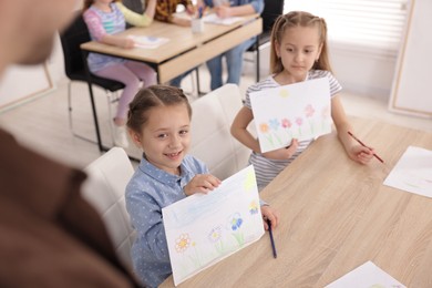 Photo of Kids showing their drawings to teacher at painting lesson indoors, selective focus