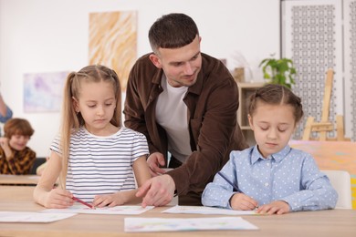 Photo of Man teaching kids to draw at painting lesson indoors