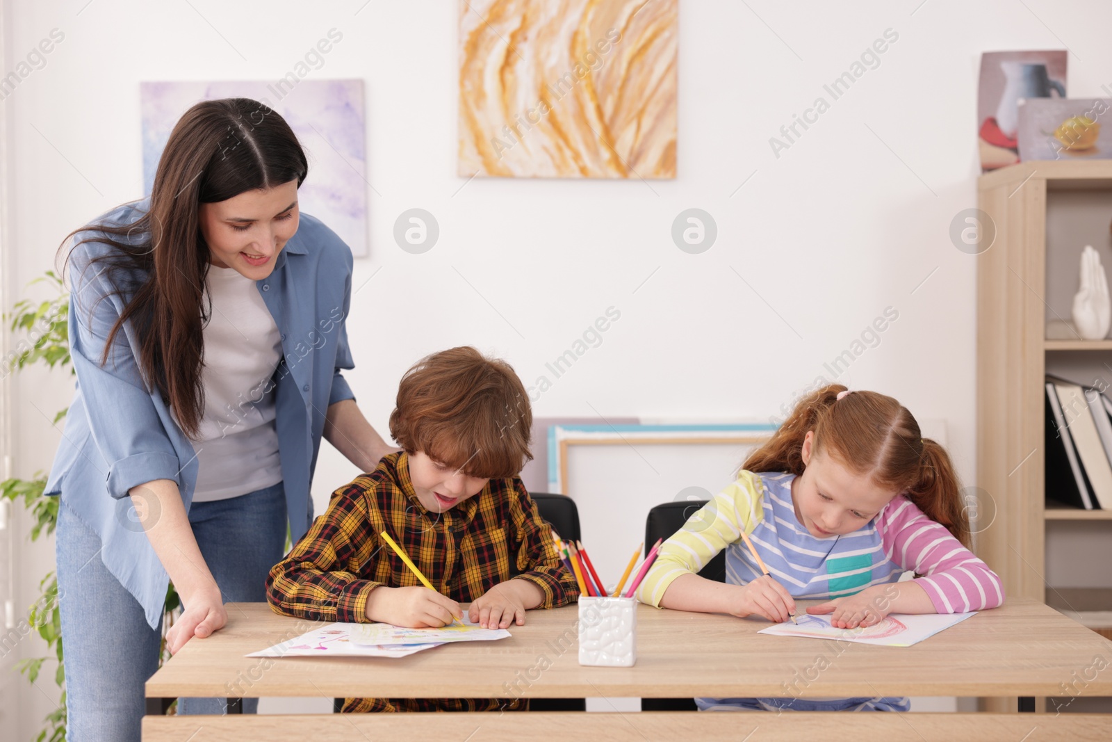 Woman teaching kids to draw at painting lesson indoors Photo of Woman teaching kids to draw at painting lesson indoors
