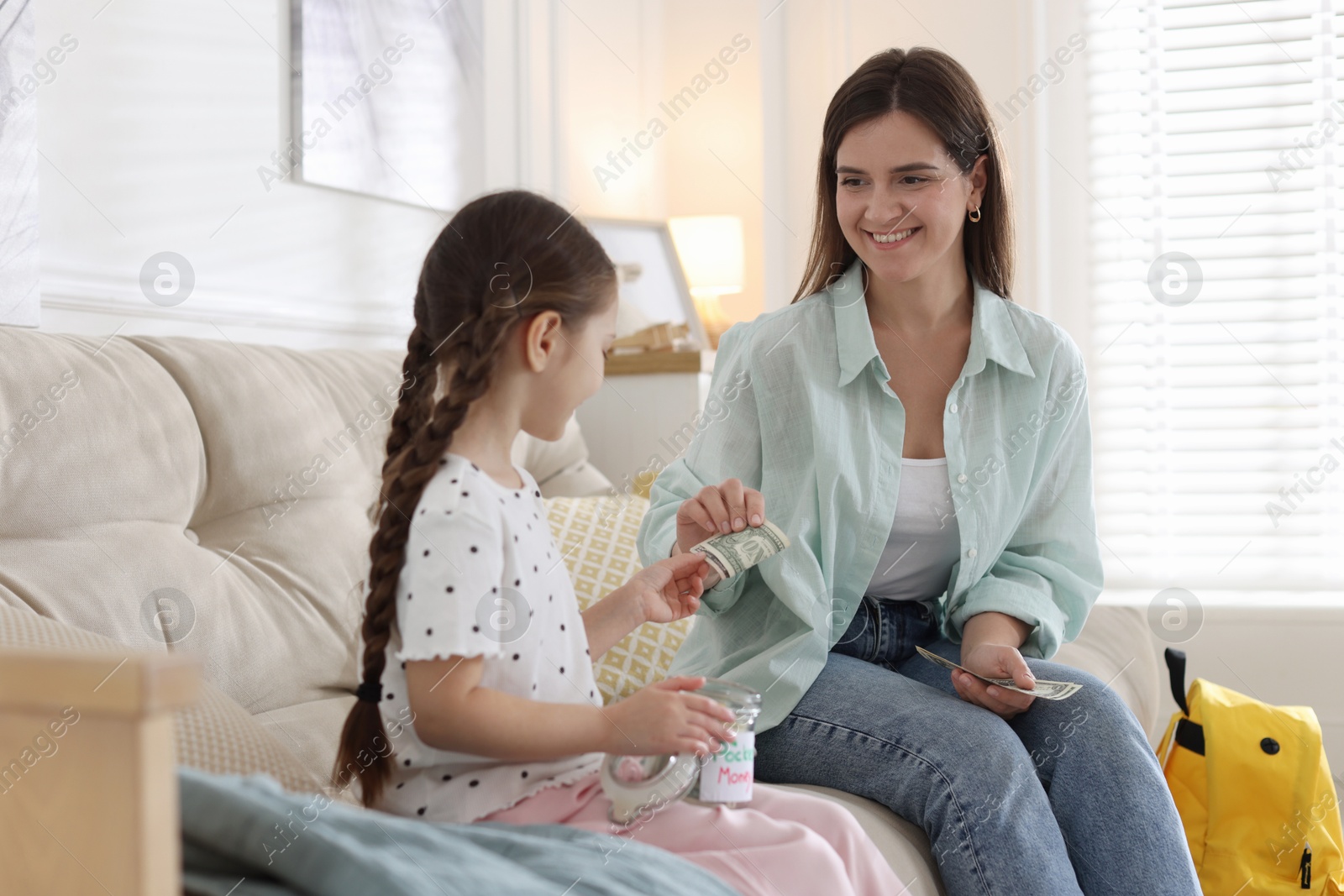 Mother giving pocket money to her daughter on sofa at home Photo of Mother giving pocket money to her daughter on sofa at home
