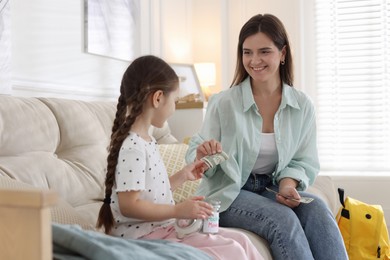 Photo of Mother giving pocket money to her daughter on sofa at home
