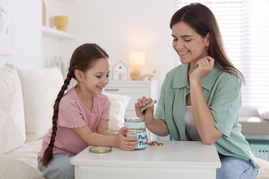 Photo of Mother giving her daughter pocket money at table indoors
