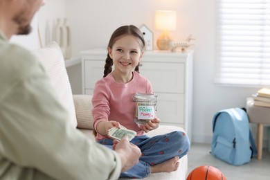 Photo of Father giving his daughter pocket money on sofa at home, closeup