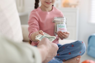 Photo of Father giving his daughter pocket money on sofa at home, closeup