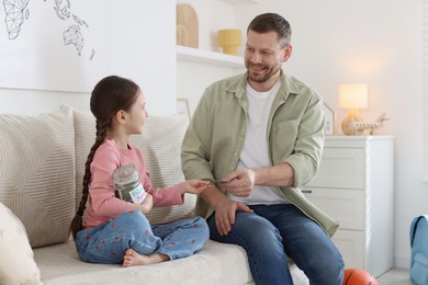 Photo of Father giving his daughter pocket money on sofa at home