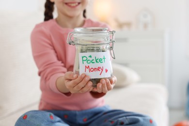 Photo of Girl with jar of pocket money on sofa at home, closeup