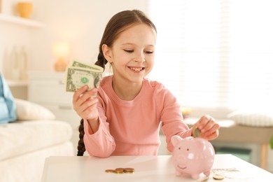 Photo of Girl putting her pocket money into piggybank at table indoors