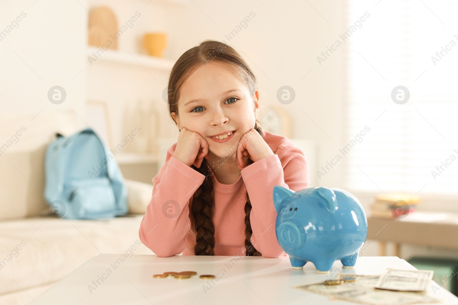 Girl with piggybank of pocket money at table indoors Photo of Girl with piggybank of pocket money at table indoors