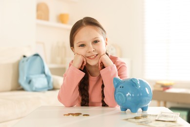 Photo of Girl with piggybank of pocket money at table indoors