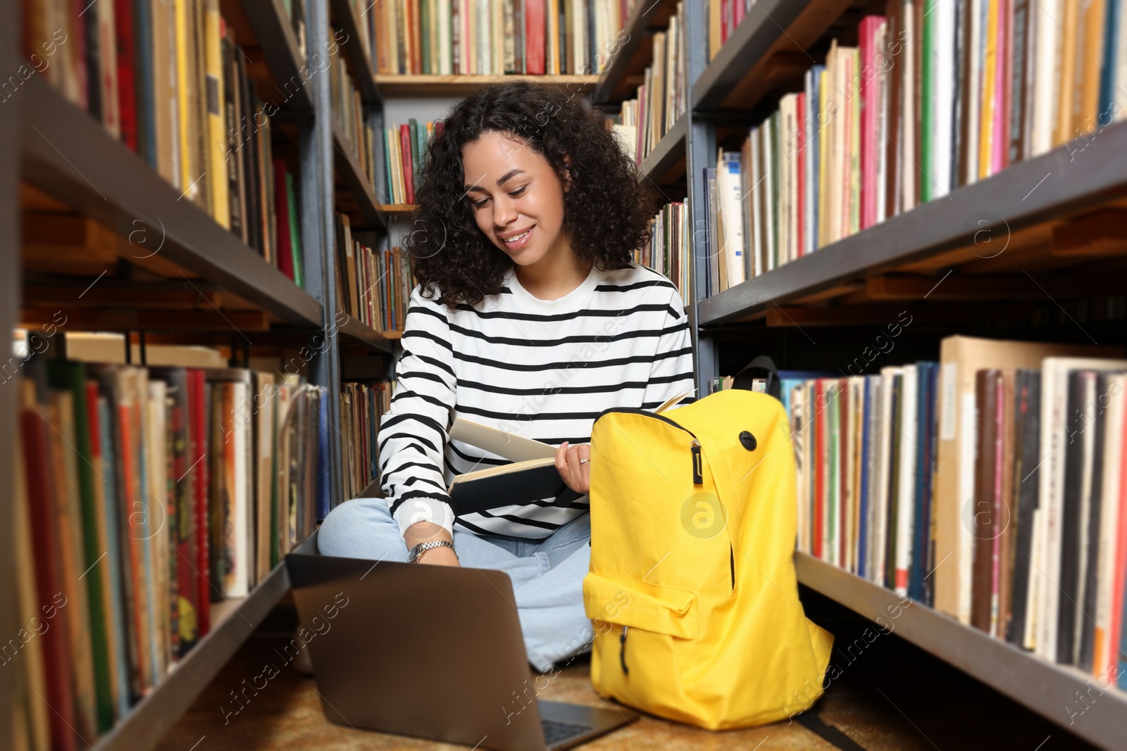Woman with book studying near shelves in public library Photo of Woman with book studying near shelves in public library