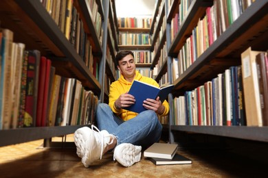 Photo of Man reading book near shelves in public library, low angle view
