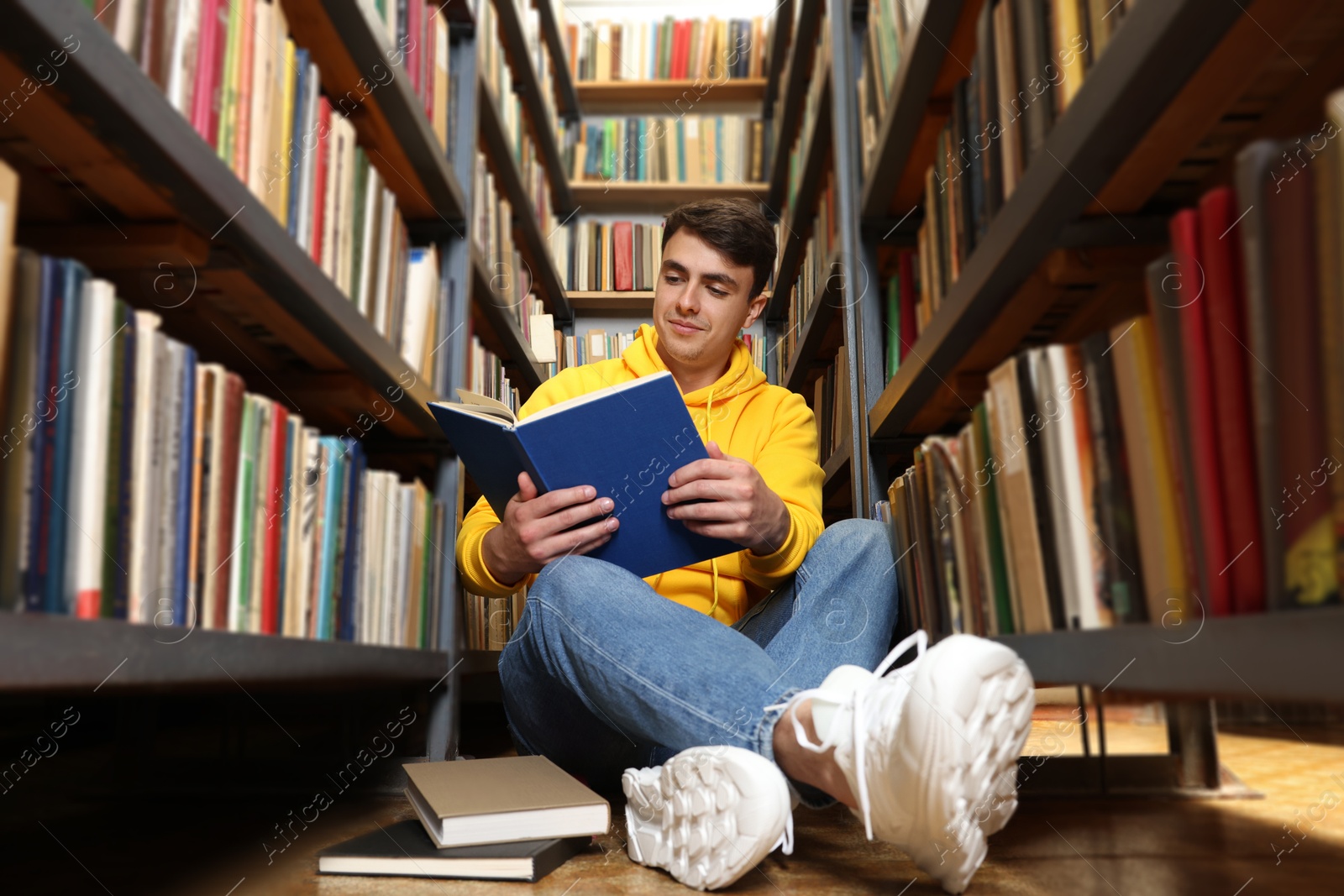 Man reading book near shelves in public library, low angle view Photo of Man reading book near shelves in public library, low angle view