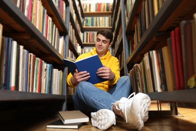 Photo of Man reading book near shelves in public library, low angle view