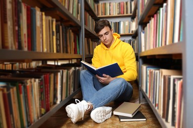 Photo of Man reading book near shelves in public library
