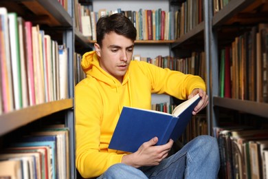 Photo of Man reading book near shelves in public library