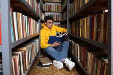 Photo of Man reading book near shelves in public library