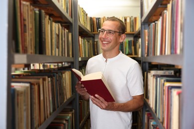 Photo of Man with book near shelves in public library