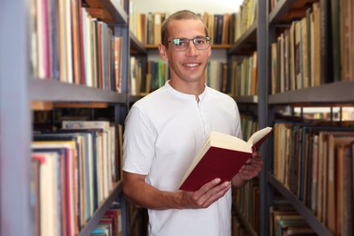 Photo of Man with book near shelves in public library