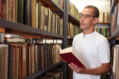 Photo of Man with book near shelves in public library