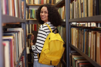 Photo of Woman with laptop and backpack near shelves in public library