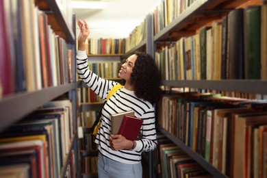 Photo of Woman with books and backpack near shelves in public library