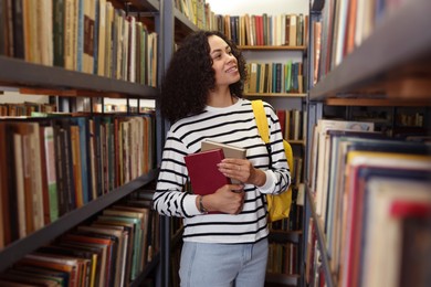 Photo of Woman with books and backpack near shelves in public library