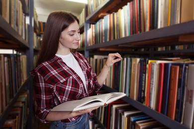 Photo of Woman with book near shelves in public library