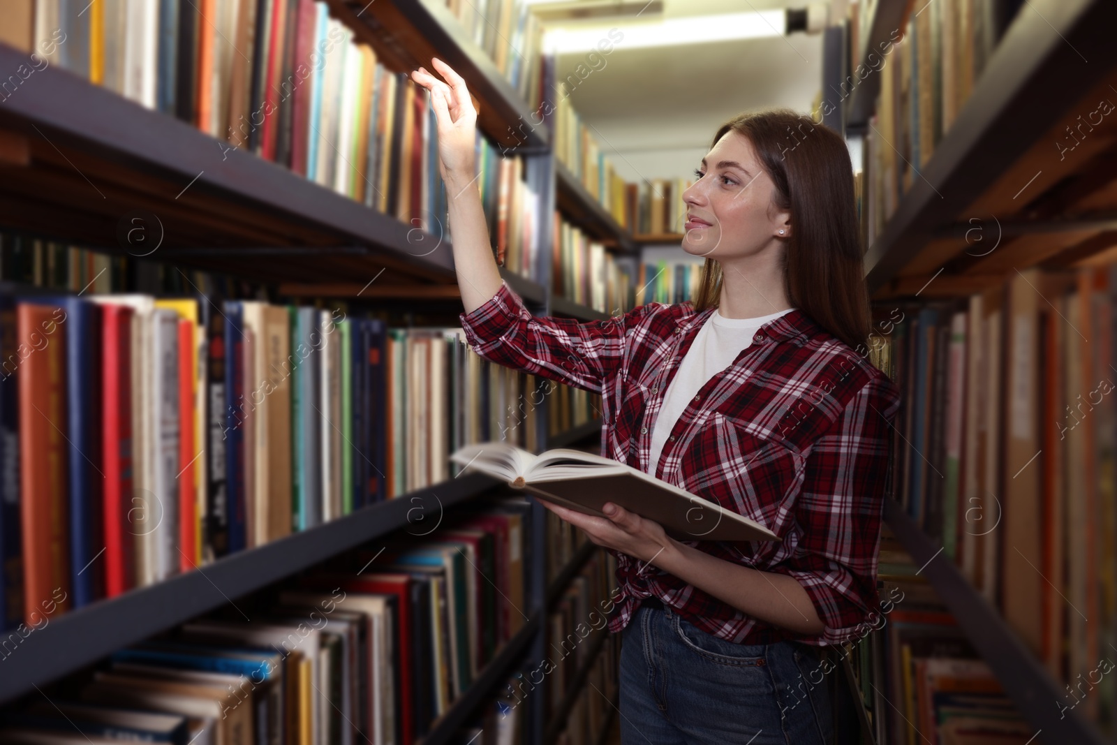 Woman with book near shelves in public library Photo of Woman with book near shelves in public library