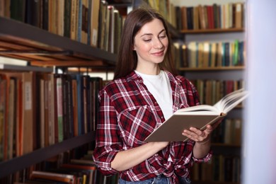 Photo of Woman reading book near shelves in public library