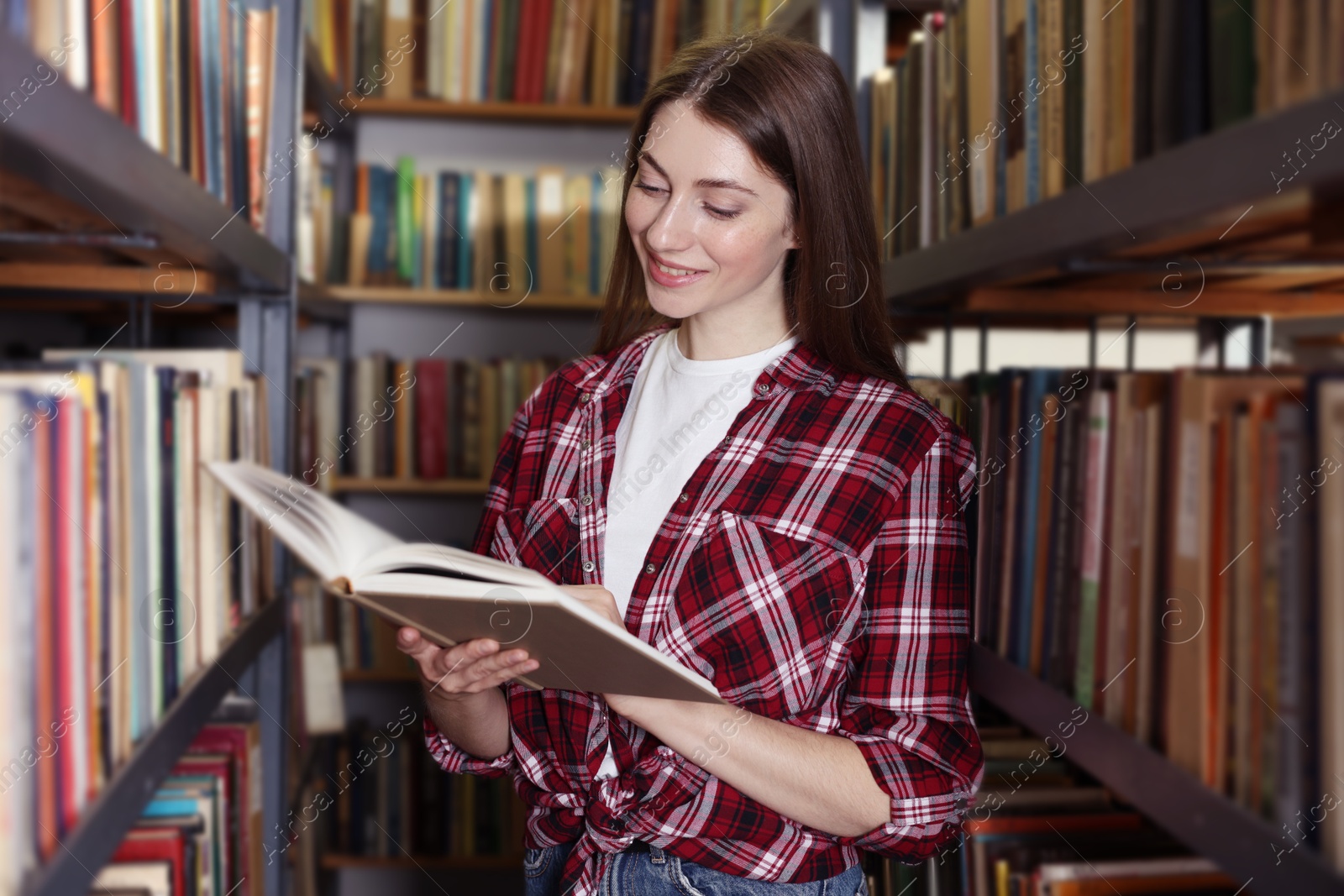 Woman reading book near shelves in public library Photo of Woman reading book near shelves in public library
