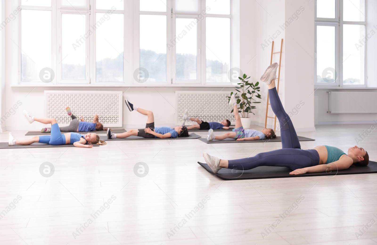 Group of children practicing yoga with coach on mats in class Photo of Group of children practicing yoga with coach on mats in class