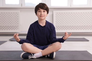 Photo of Cute boy practicing yoga on mat indoors