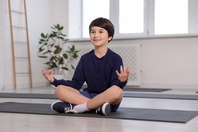 Photo of Happy boy practicing yoga on mat indoors