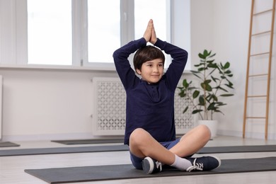 Photo of Cute boy practicing yoga on mat indoors