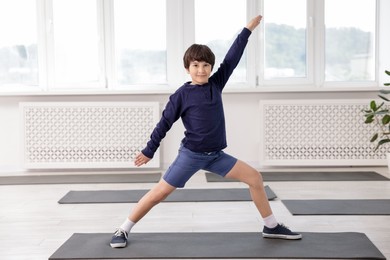 Photo of Cute boy practicing yoga on mat indoors