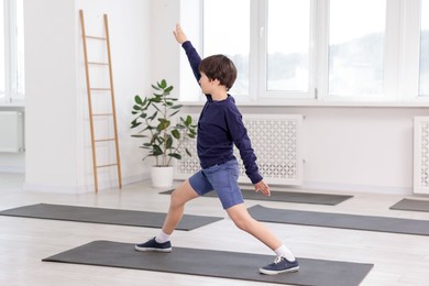 Photo of Cute boy practicing yoga on mat indoors