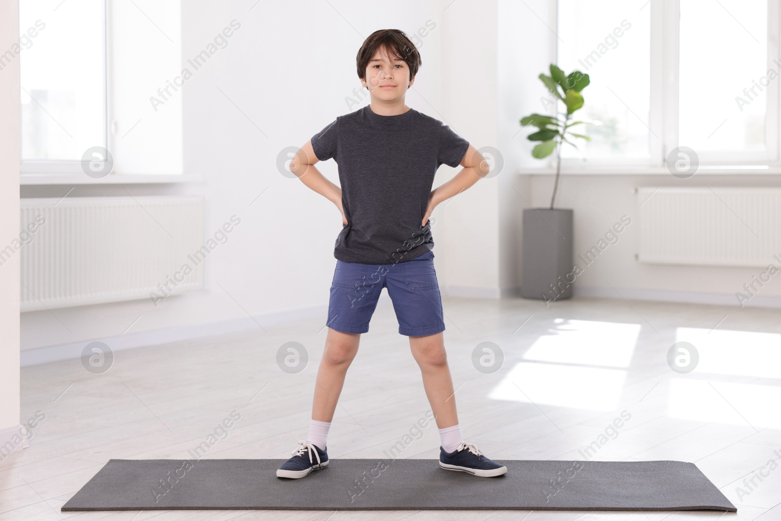 Cute boy standing on yoga mat indoors Photo of Cute boy standing on yoga mat indoors