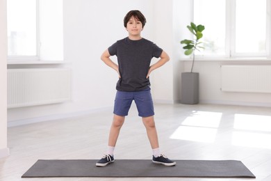 Photo of Cute boy standing on yoga mat indoors