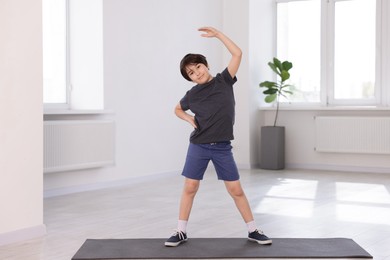 Photo of Cute boy exercising on yoga mat indoors