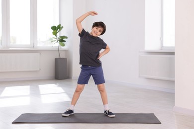 Photo of Cute boy exercising on yoga mat indoors