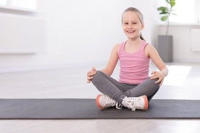 Photo of Happy girl sitting on yoga mat indoors
