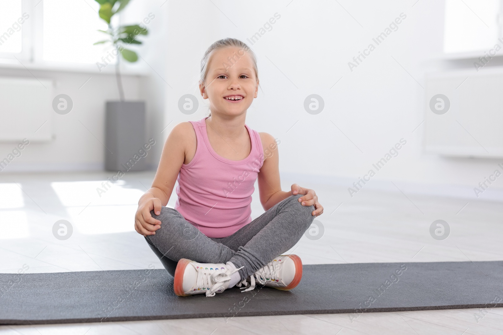 Happy girl sitting on yoga mat indoors Photo of Happy girl sitting on yoga mat indoors