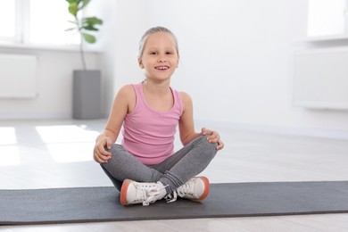 Photo of Happy girl sitting on yoga mat indoors