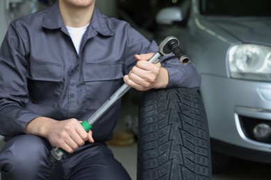 Photo of Mechanic with wrench and tire at car service, closeup
