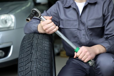 Photo of Mechanic with wrench and tire at car service, closeup