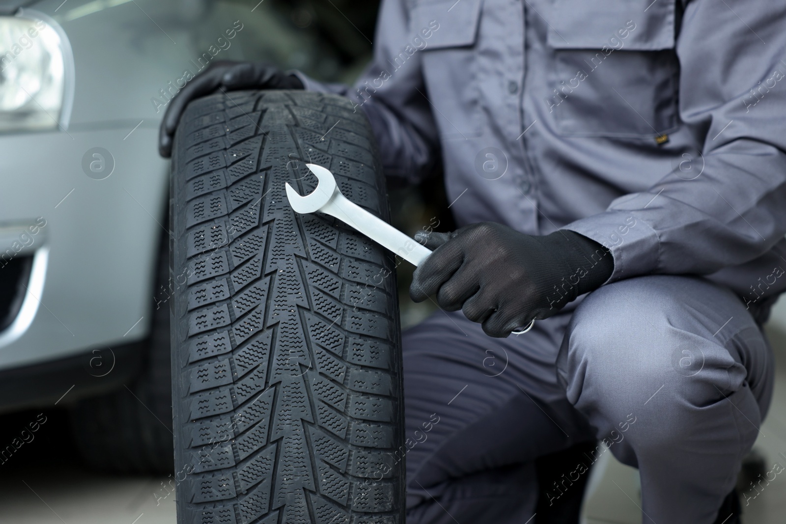 Mechanic with wrench and tire at car service, closeup Photo of Mechanic with wrench and tire at car service, closeup