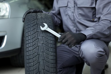 Photo of Mechanic with wrench and tire at car service, closeup