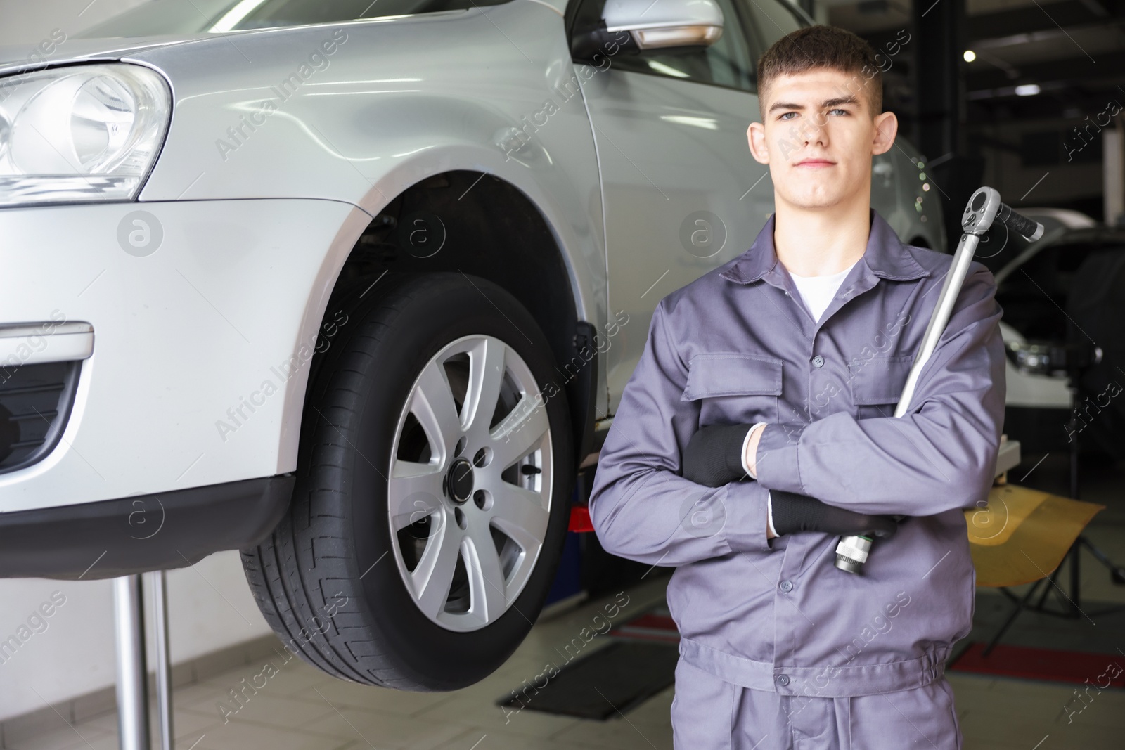 Professional mechanic with wrench near lifted car in garage Photo of Professional mechanic with wrench near lifted car in garage