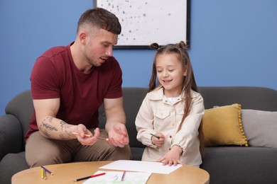 Photo of Father teaching his daughter to draw at table indoors