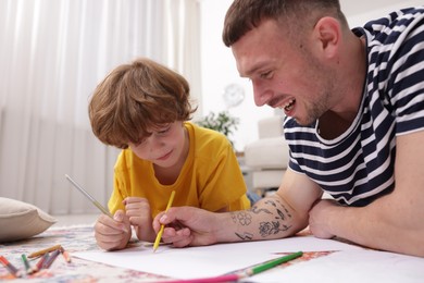 Photo of Father teaching his son to draw on floor at home